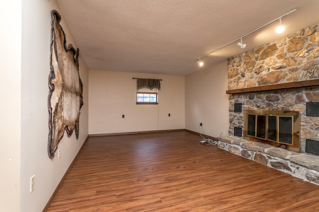 unfurnished living room with a stone fireplace, hardwood / wood-style floors, rail lighting, and a textured ceiling