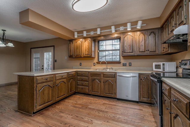 kitchen featuring wood-type flooring, kitchen peninsula, sink, appliances with stainless steel finishes, and decorative light fixtures