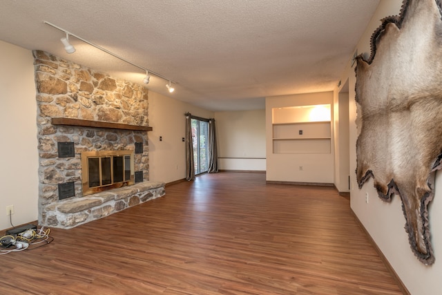 unfurnished living room with hardwood / wood-style floors, a stone fireplace, a textured ceiling, and rail lighting