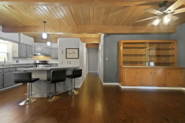 kitchen featuring gray cabinetry, dark hardwood / wood-style flooring, stainless steel range, and a breakfast bar area