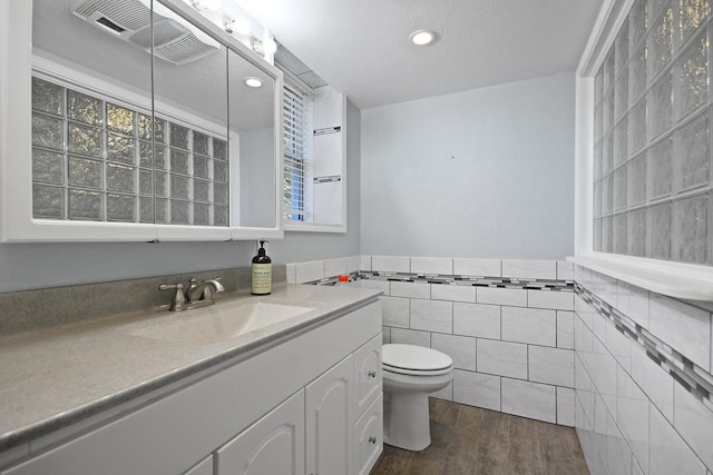 bathroom with hardwood / wood-style flooring, vanity, tile walls, and toilet