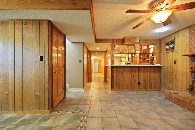 kitchen featuring kitchen peninsula, ceiling fan, wood walls, and light tile patterned floors