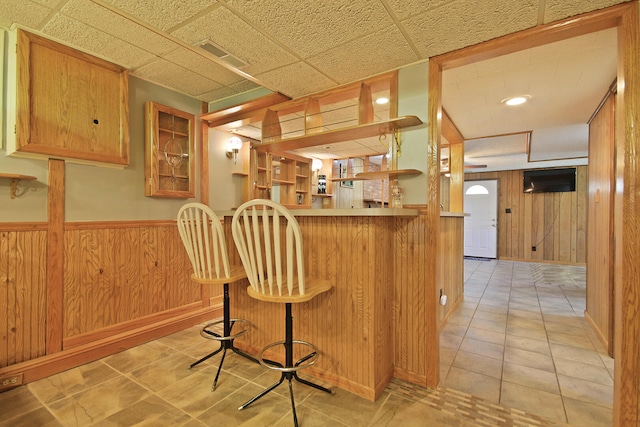 kitchen featuring light tile patterned floors, a breakfast bar area, wooden walls, and kitchen peninsula