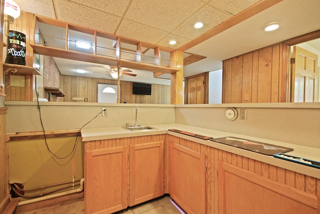 kitchen featuring wood walls, a drop ceiling, ceiling fan, sink, and light tile patterned floors