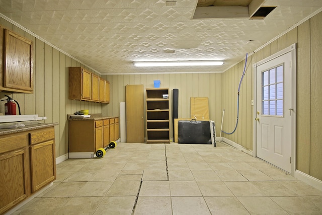 kitchen with light tile patterned floors, wood walls, and ornamental molding