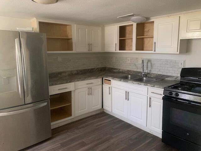 kitchen with dark wood-type flooring, black gas stove, sink, stainless steel fridge, and white cabinetry