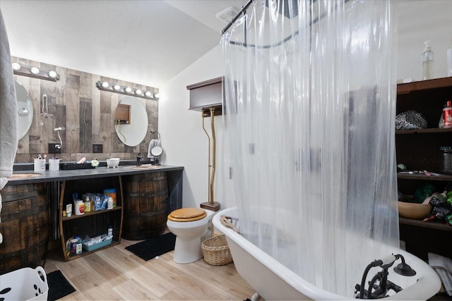 bathroom with hardwood / wood-style floors, vanity, wooden walls, vaulted ceiling, and toilet