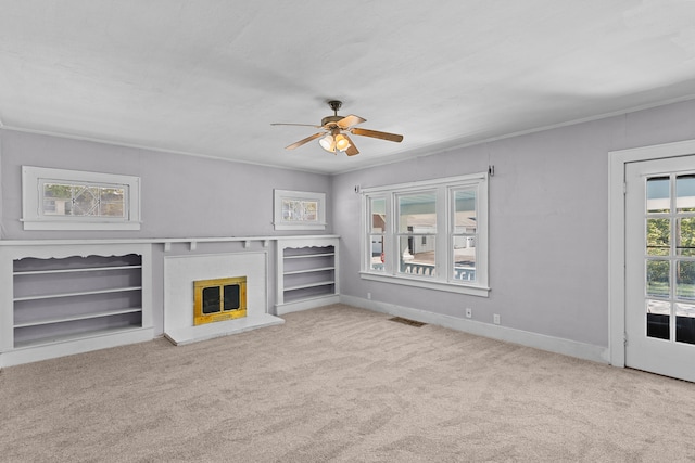 unfurnished living room featuring ornamental molding, a brick fireplace, ceiling fan, and light colored carpet