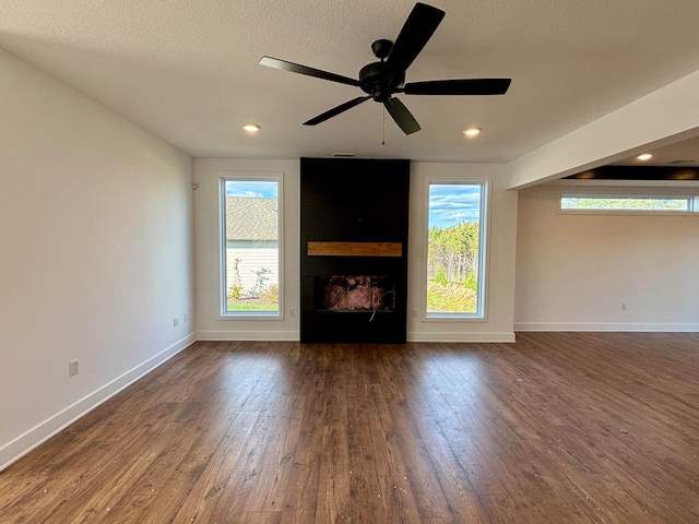 unfurnished living room featuring a wealth of natural light, a large fireplace, baseboards, and dark wood-style flooring