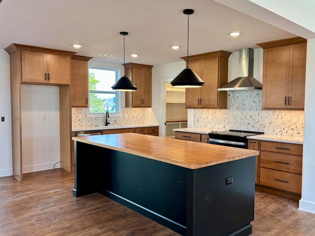 kitchen featuring electric stove, brown cabinets, a kitchen island, wall chimney range hood, and wood counters