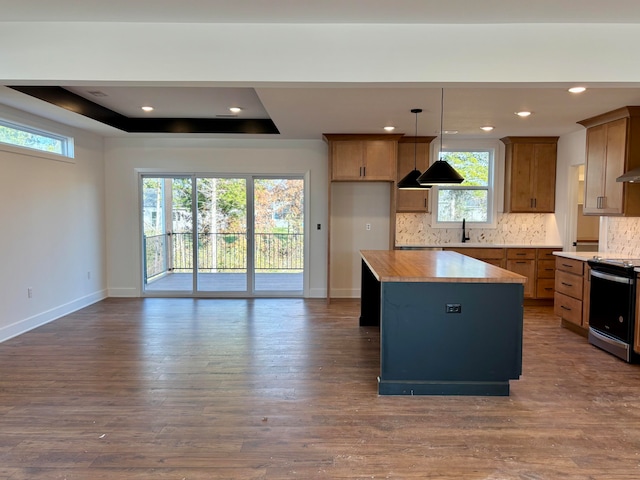 kitchen featuring electric stove, a center island, brown cabinetry, a raised ceiling, and pendant lighting