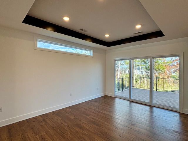 empty room with dark wood-style floors, a raised ceiling, visible vents, and baseboards