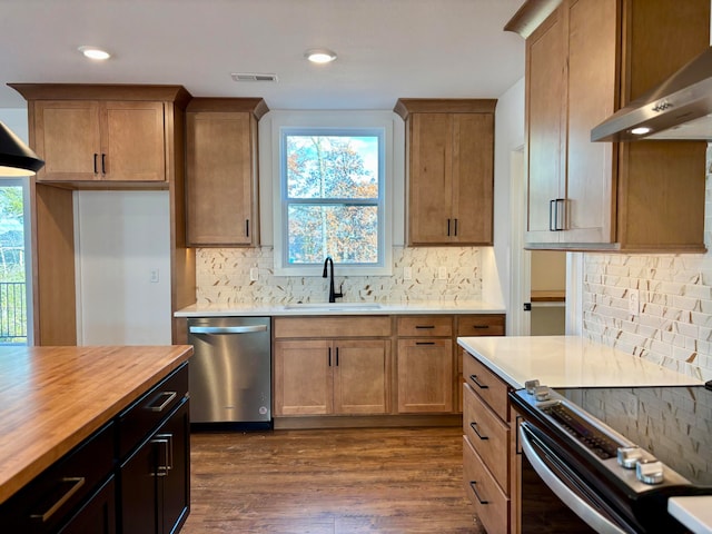 kitchen featuring visible vents, dark wood-style floors, appliances with stainless steel finishes, wall chimney range hood, and a sink