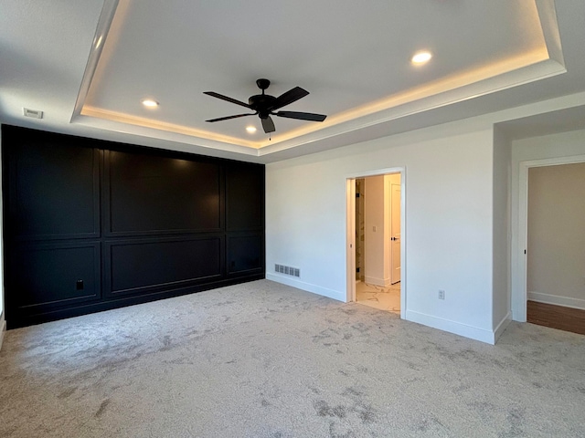 unfurnished bedroom featuring a raised ceiling, visible vents, light carpet, and baseboards