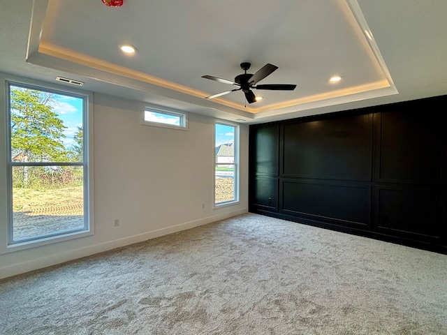 unfurnished bedroom with carpet floors, a ceiling fan, visible vents, baseboards, and a raised ceiling