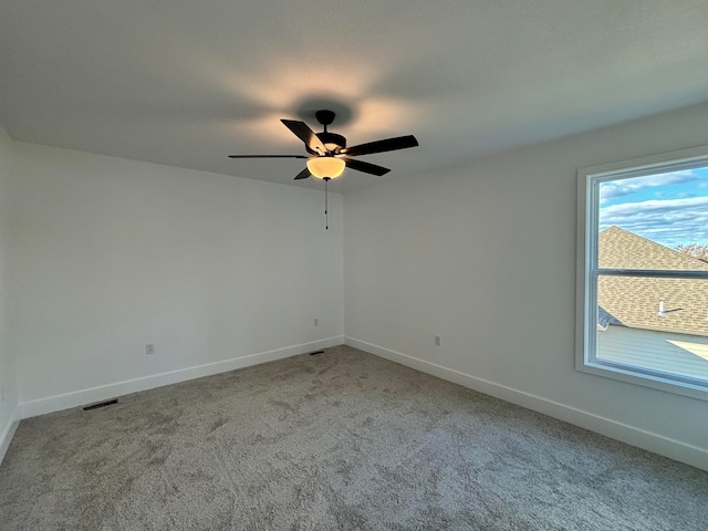 carpeted spare room with visible vents, baseboards, and ceiling fan