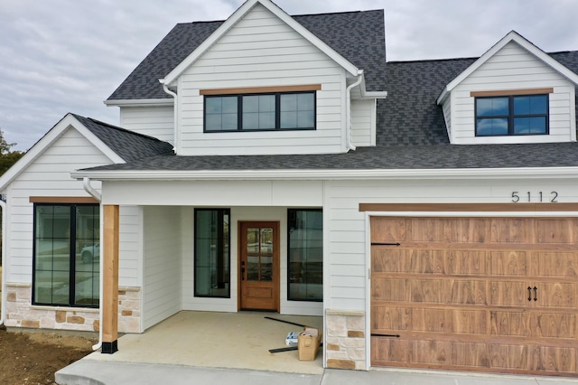 view of front of home featuring a porch, stone siding, roof with shingles, and a garage