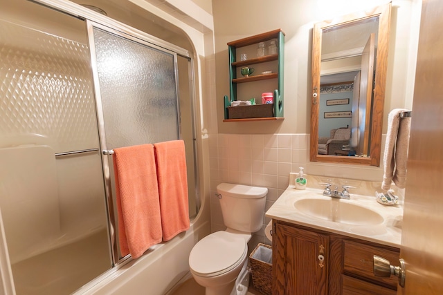 full bathroom featuring bath / shower combo with glass door, vanity, tile walls, and toilet