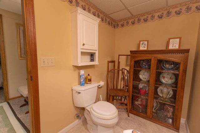 bathroom with a drop ceiling, tile patterned flooring, and toilet