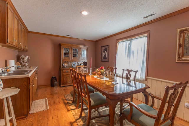 dining room featuring a textured ceiling, light wood-type flooring, crown molding, and sink