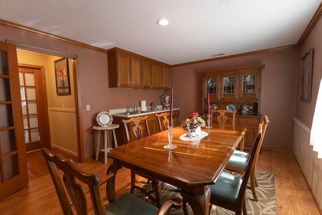 dining room with ornamental molding, wood walls, light hardwood / wood-style floors, and a textured ceiling