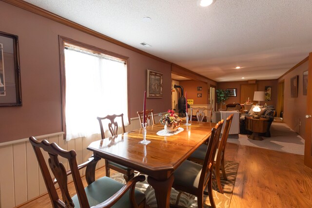 dining area featuring ornamental molding, light wood-type flooring, and a textured ceiling