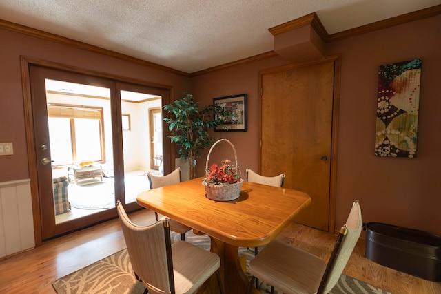 dining space featuring crown molding, light hardwood / wood-style flooring, and a textured ceiling