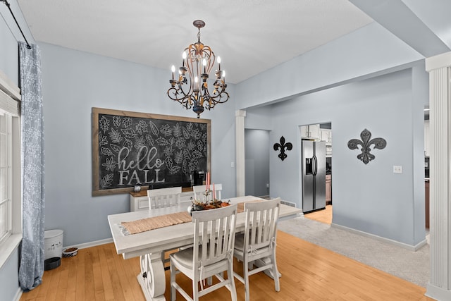 dining space with a chandelier, decorative columns, and light wood-type flooring