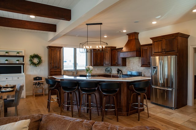 kitchen featuring hanging light fixtures, custom exhaust hood, stainless steel fridge with ice dispenser, a chandelier, and a kitchen island with sink