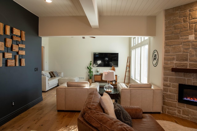 living room with beam ceiling, a stone fireplace, light hardwood / wood-style floors, and wood ceiling