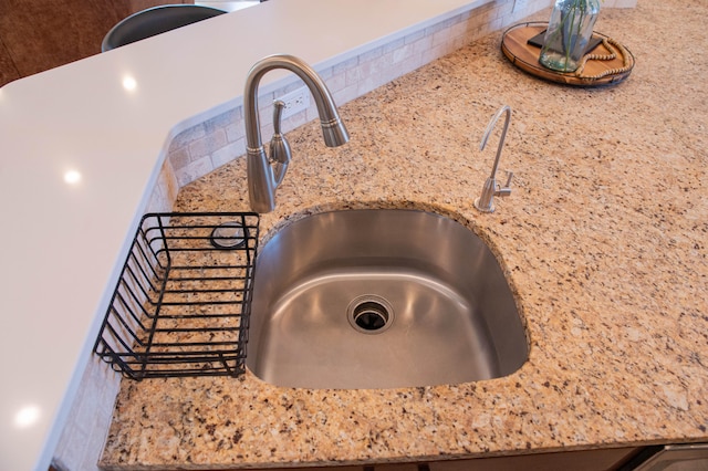 room details featuring light stone counters, sink, and backsplash