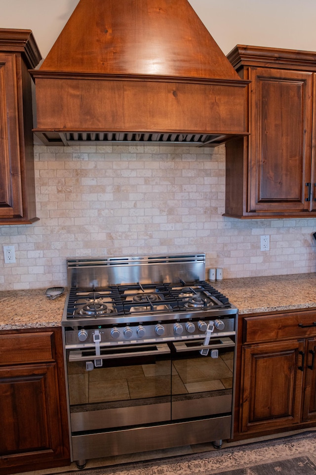 kitchen with light stone counters, high end stainless steel range, decorative backsplash, and custom exhaust hood