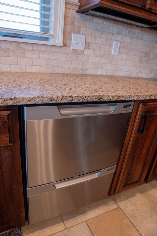 room details with decorative backsplash, stainless steel dishwasher, light stone counters, and light tile patterned floors