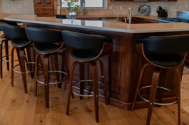 bar with stove, decorative backsplash, light wood-type flooring, and sink