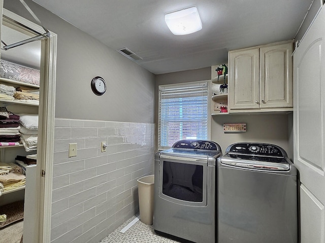 laundry area with tile walls, washing machine and clothes dryer, light tile patterned floors, and cabinets