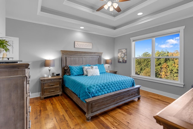 bedroom featuring a raised ceiling, ornamental molding, light wood-type flooring, and ceiling fan