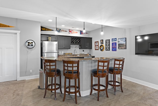 kitchen with a breakfast bar area, stainless steel fridge, a center island, pendant lighting, and stone counters