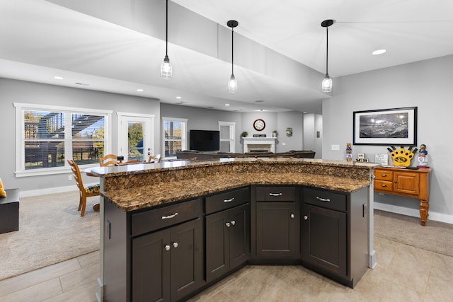 kitchen with a center island, hanging light fixtures, light colored carpet, and dark stone counters