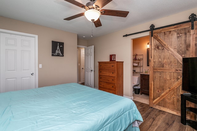 bedroom featuring ceiling fan, a textured ceiling, a barn door, wood-type flooring, and ensuite bathroom