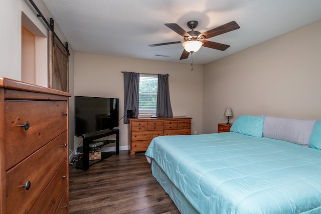 bedroom featuring a textured ceiling, a barn door, dark wood-type flooring, and ceiling fan