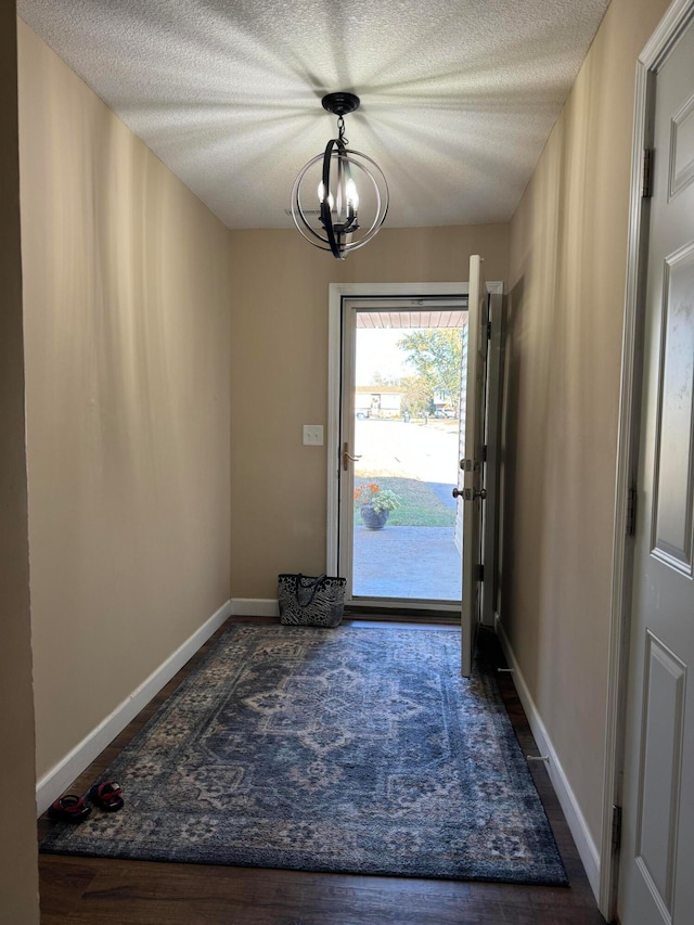 doorway with a notable chandelier, a textured ceiling, and dark hardwood / wood-style flooring