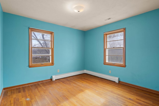 spare room featuring baseboard heating, a healthy amount of sunlight, and light hardwood / wood-style floors