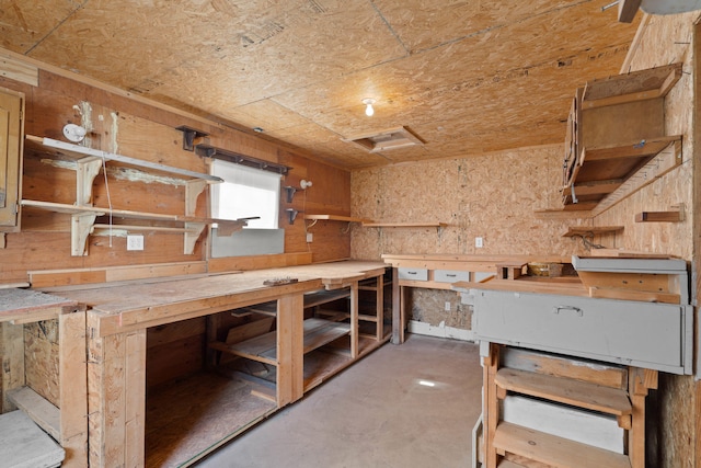 miscellaneous room with a workshop area, wooden walls, and concrete floors