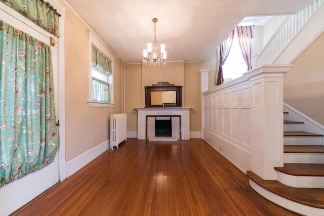 unfurnished living room featuring dark wood-type flooring, radiator heating unit, crown molding, and a notable chandelier