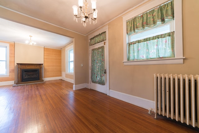 unfurnished living room featuring ornamental molding, wood-type flooring, radiator heating unit, and a chandelier