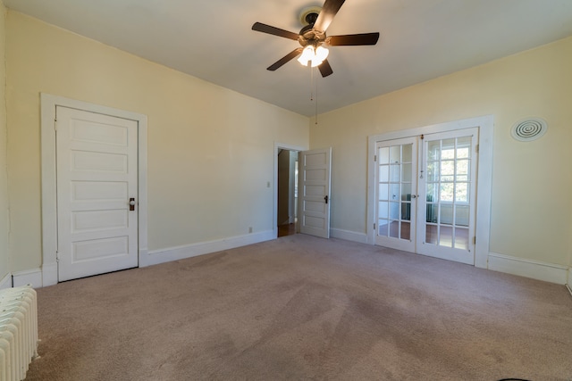 carpeted spare room featuring radiator, ceiling fan, and french doors