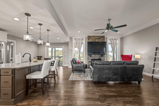 living room featuring ceiling fan, a stone fireplace, ornamental molding, and dark hardwood / wood-style floors