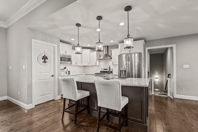 kitchen with appliances with stainless steel finishes, wall chimney exhaust hood, white cabinets, and decorative light fixtures