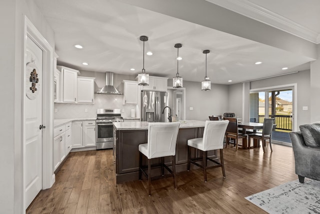 kitchen featuring stainless steel appliances, wall chimney exhaust hood, pendant lighting, dark wood-type flooring, and a center island with sink