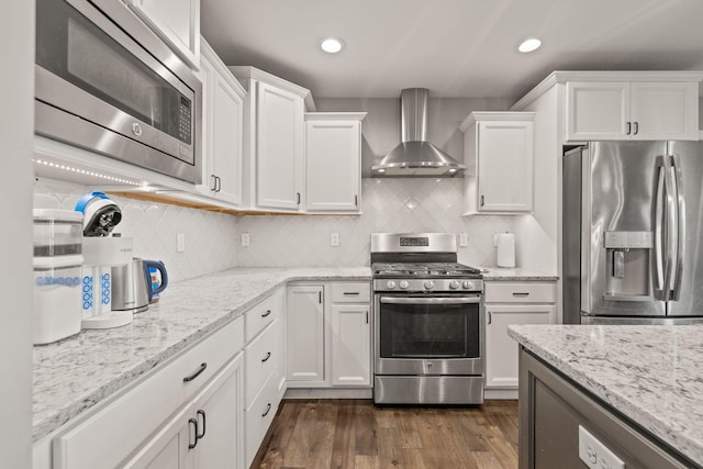 kitchen featuring appliances with stainless steel finishes, white cabinetry, dark wood-type flooring, and wall chimney range hood